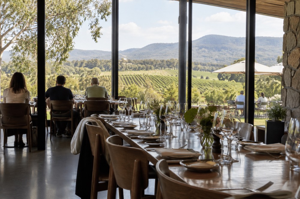 A long table set for lunch inside a winery restaurant with windows facing the vines