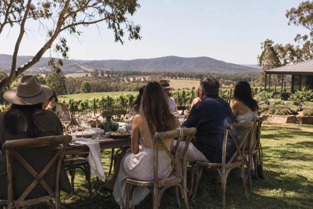 A long table set for lunch on a winery lawn overlooking vine rows