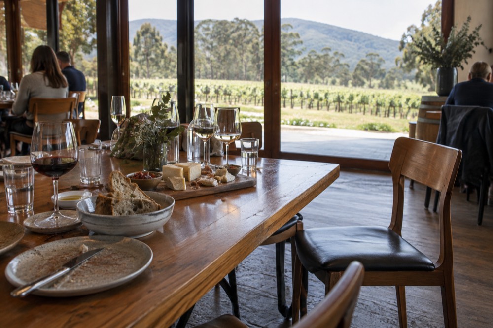 A wooden table with wine glasses, a cheese board and bread in a winery dining room