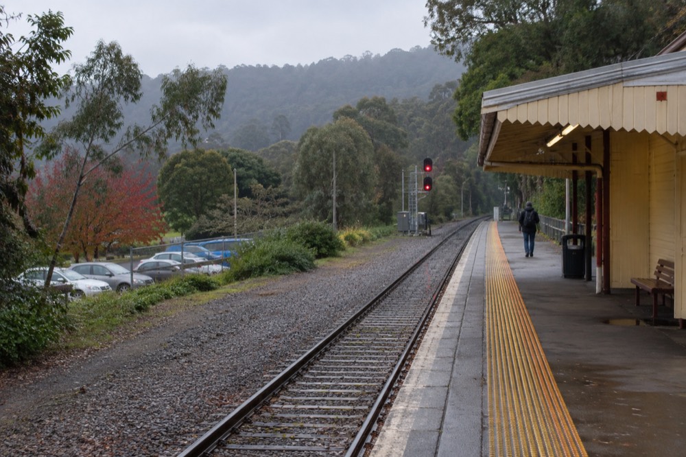 Country railway platform with a shelter and hills behind the track