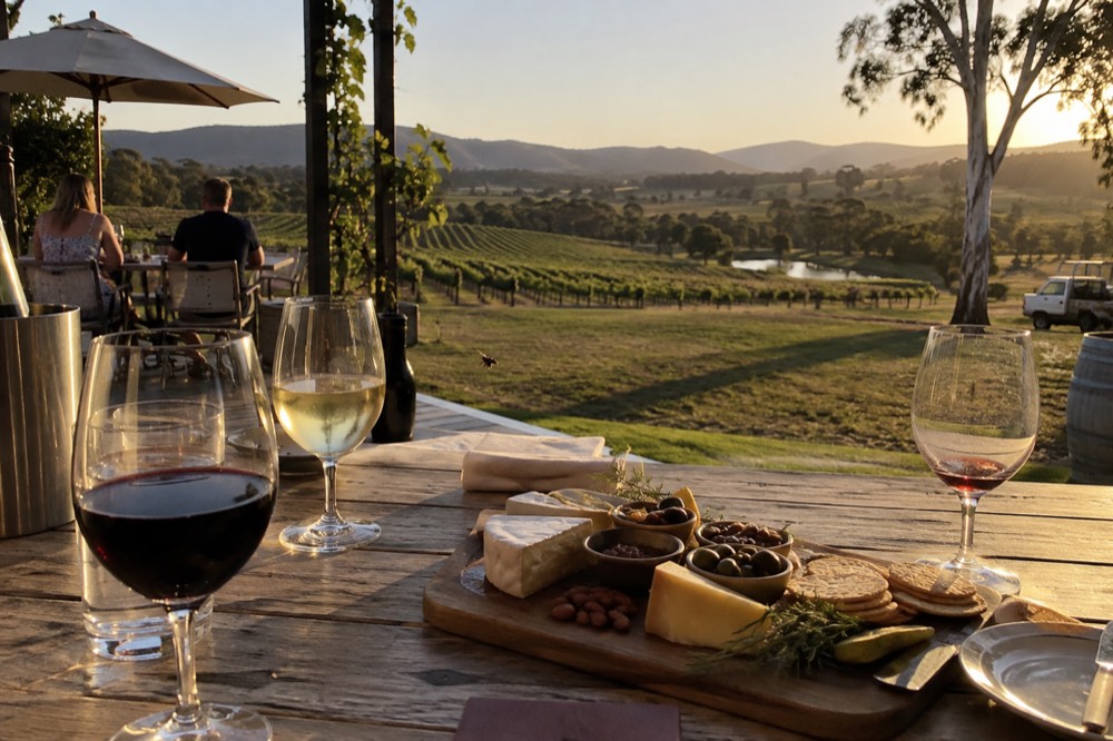 An outdoor table set with wine glasses and a grazing platter overlooking vineyards