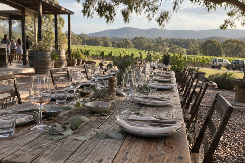 Long lunch table set with wine glasses overlooking vineyard rows in the Yarra Valley