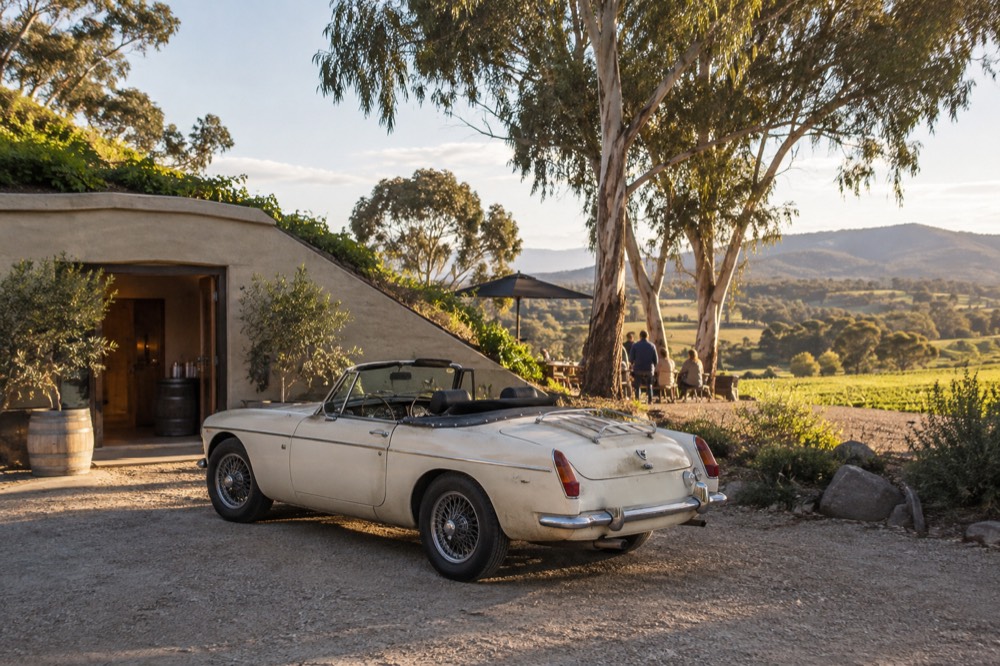 A vintage convertible car parked on a gravel drive beside a winery cellar door