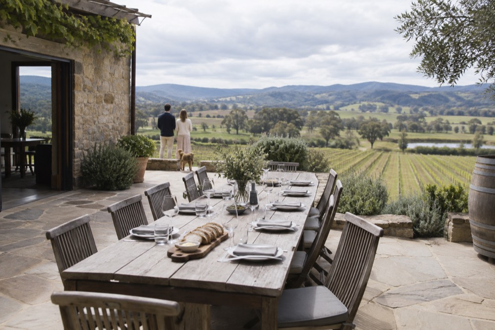 A long table set for lunch on a winery terrace overlooking vines