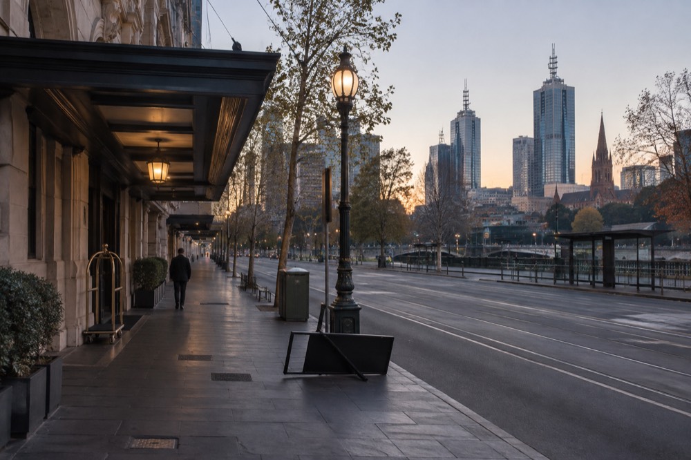 An empty city street outside a hotel at dawn with a street light still glowing