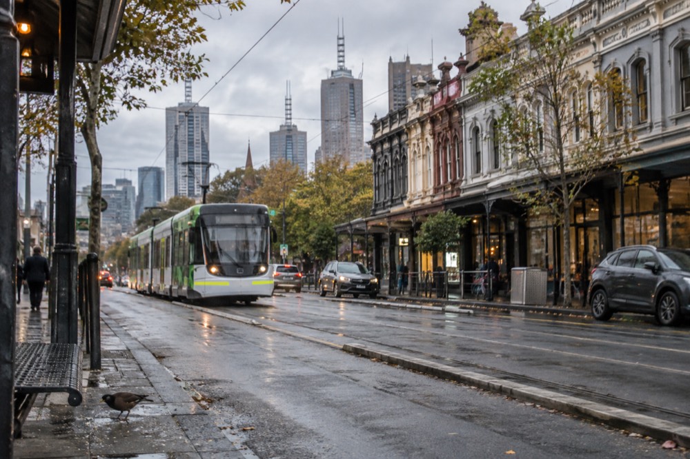 A tram moving along a Melbourne street past rows of shops in the early morning