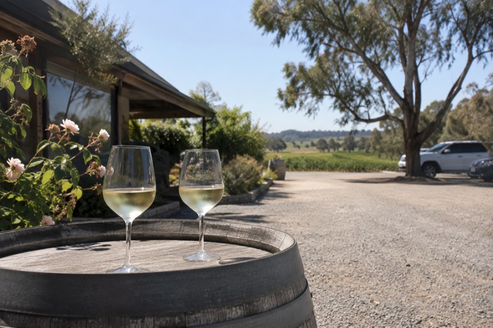 Two glasses of white wine on a barrel outside a cellar door at midday