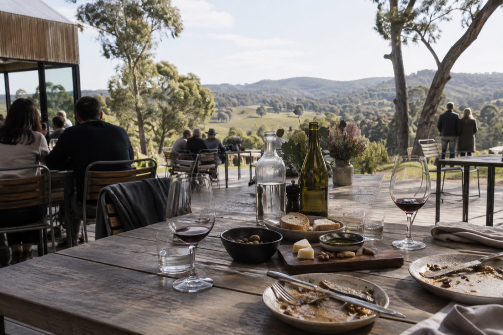 Guests seated at an outdoor winery table with wine glasses and shared plates of food