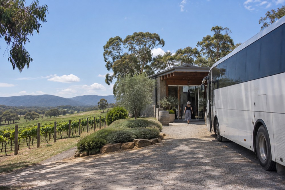 Tour coach parked on a gravel driveway beside a winery entrance at midday